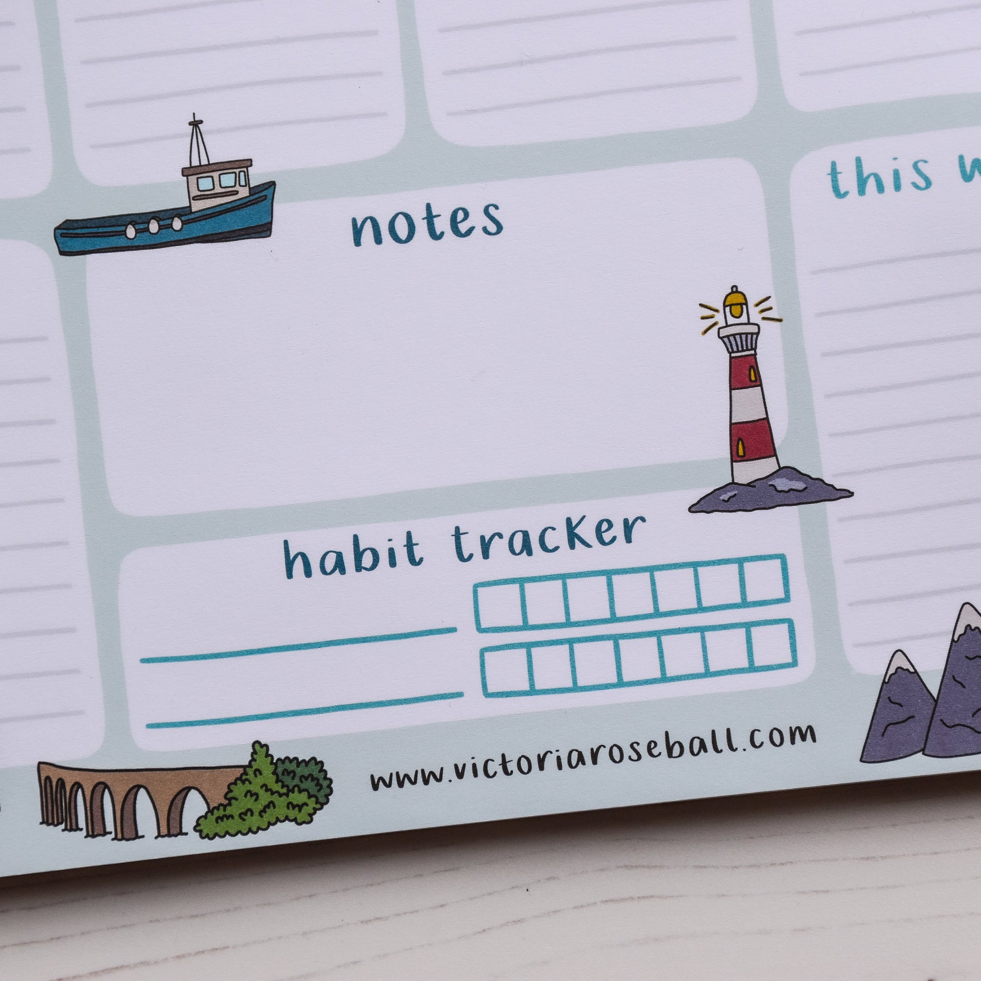 Close-up of a planner with a lighthouse, mountains and other illustrations on a white surface.