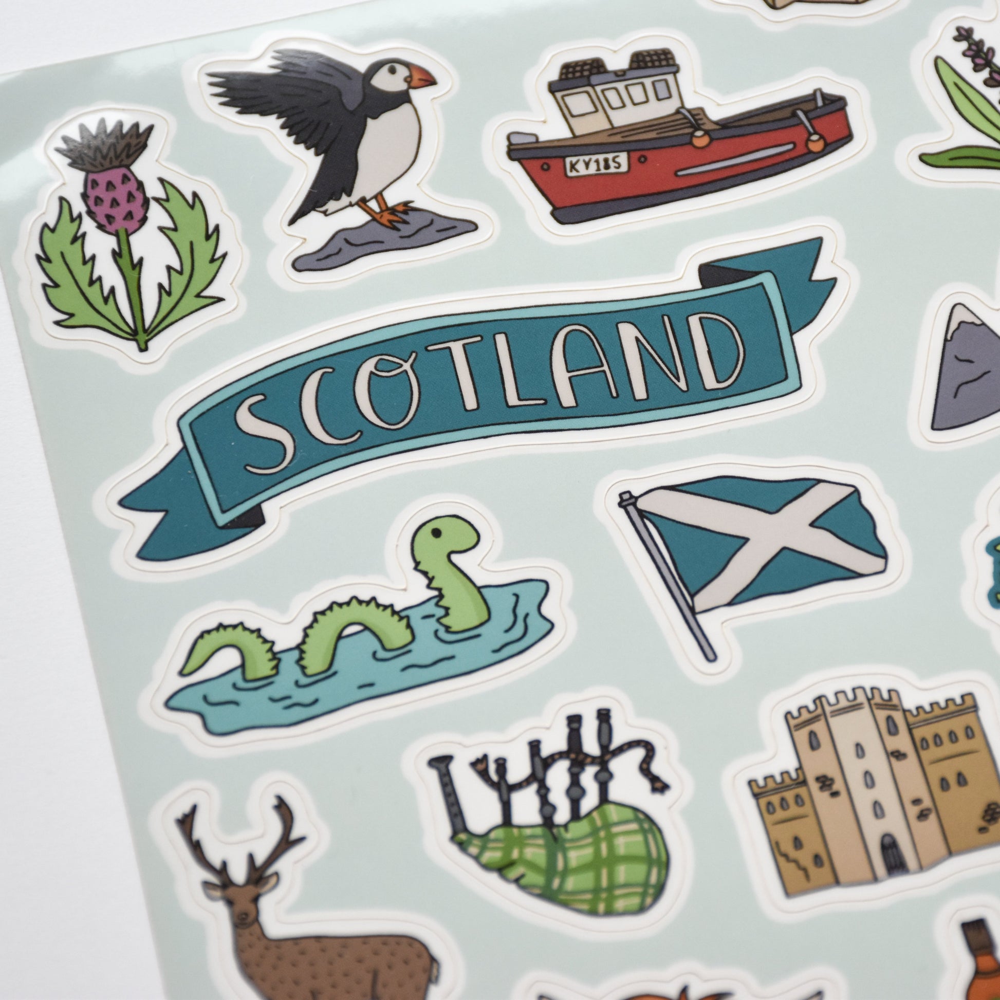Sheet of stickers with Scottish-themed designs including a castle, flag, and mountains on a light blue background.