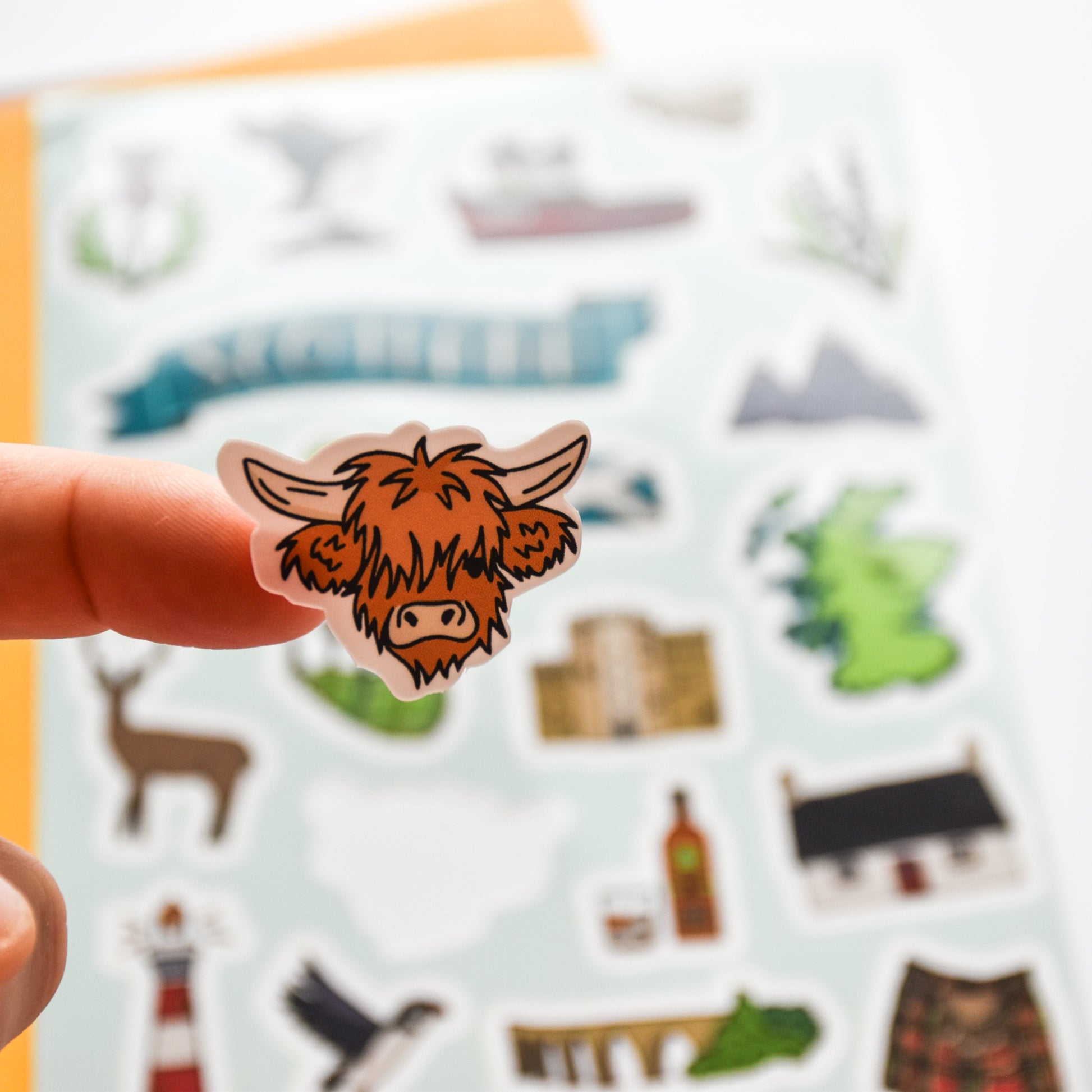 Hand holding a sticker of a cow with a colorful background of other stickers.
